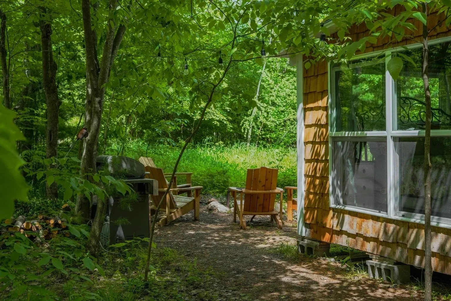 A cabin with chairs and a grill in the woods.