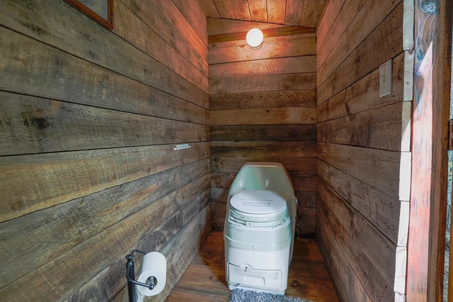 A toilet in the corner of a room with wood walls.