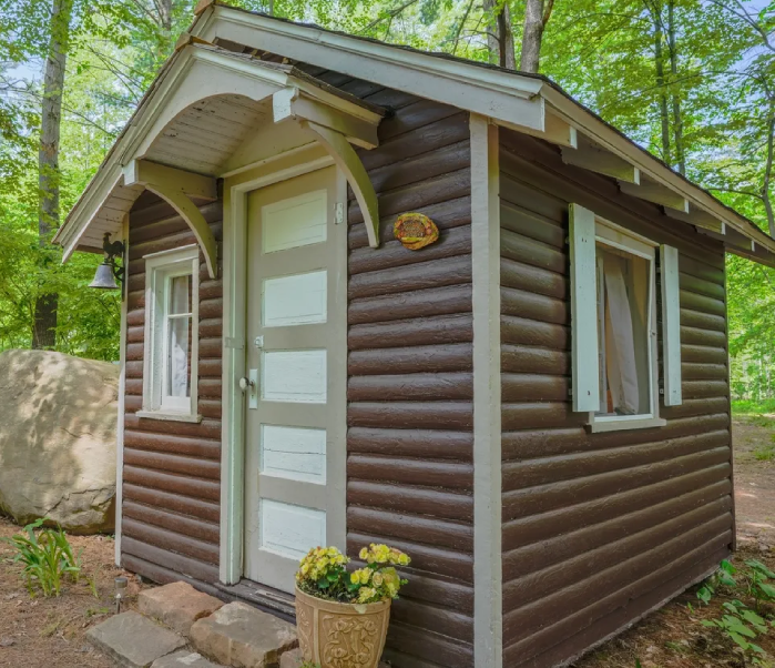 A small brown cabin in the woods with flowers.