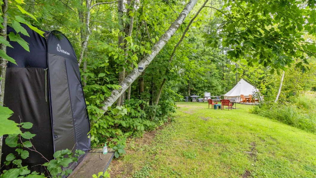 A tent in the middle of a field with trees.