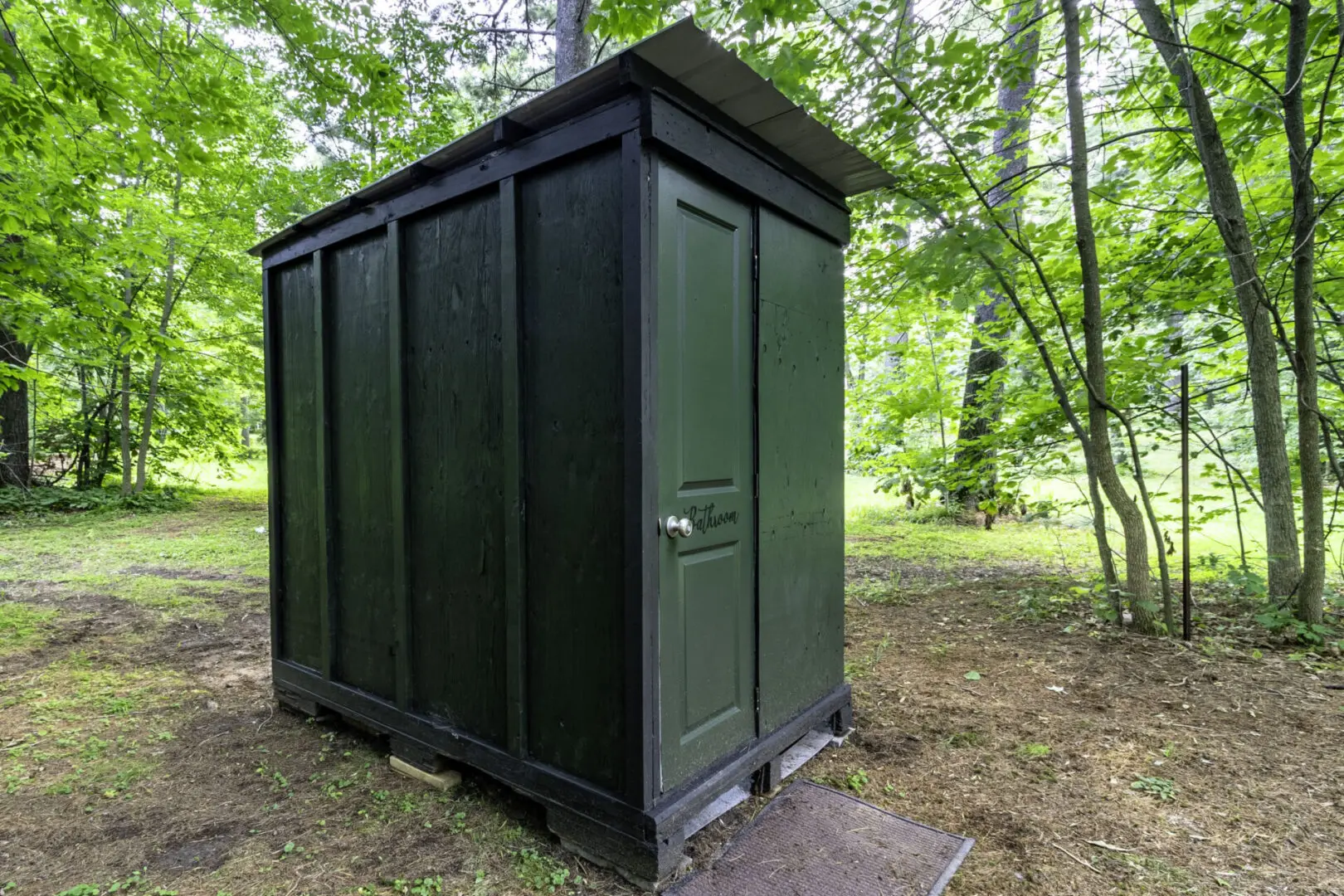 A green outhouse in the woods with trees