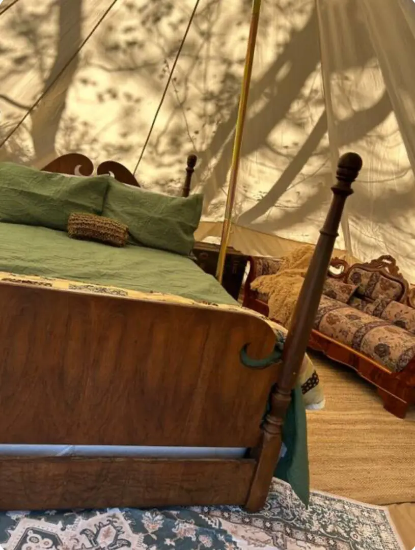 A bed with green sheets and pillows in front of a tent.