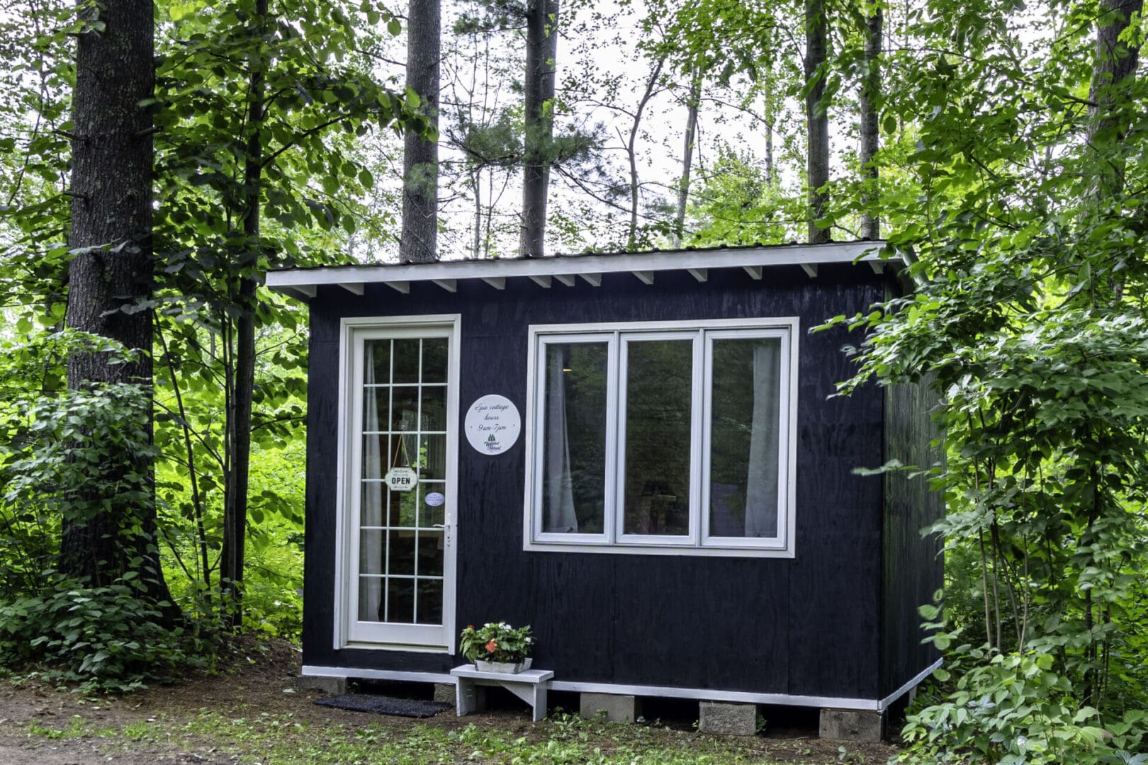 A small black house in the woods with a plaque on it.